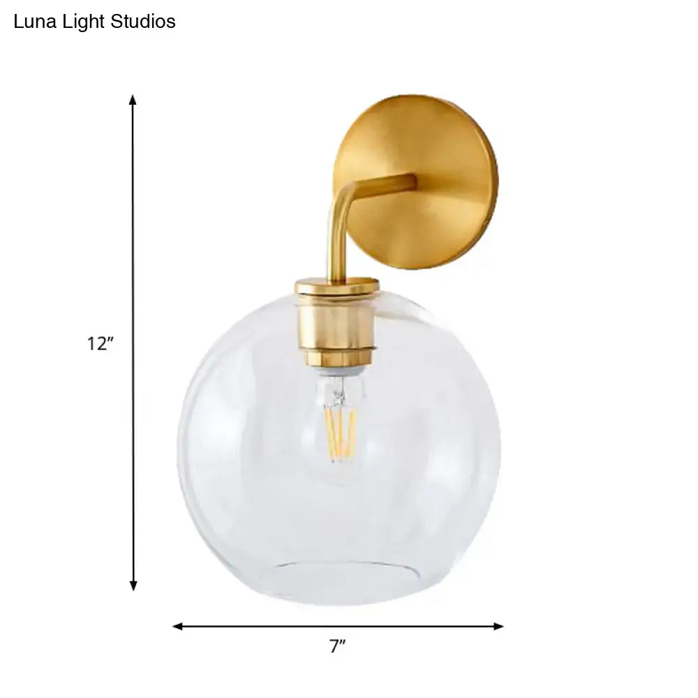 Modern brass wall lamp with gold-toned sconce and clear white glass globe featuring an exposed filament bulb for bedroom use
