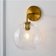 Modern brass wall lamp with sleek brass finish and clear white glass globe shade for bedroom lighting