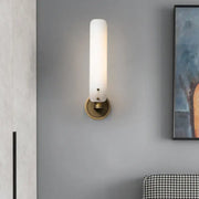 A modern brass wall lamp with a white frosted opal glass shade and brass-finished circular base for bedroom use