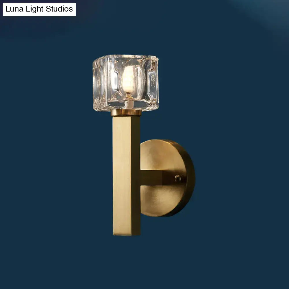 Modern brass wall light with a clear crystal block shade and sleek brass-finished metal base for living room use