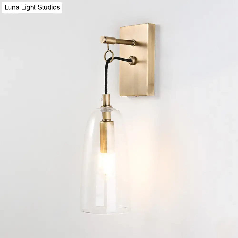 Brass-finished modern wall mount lamp with clear glass bell-shaped shade and black cord for bedroom lighting