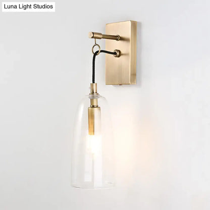 Brass-finished modern wall mount lamp with clear glass bell-shaped shade and black cord for bedroom lighting