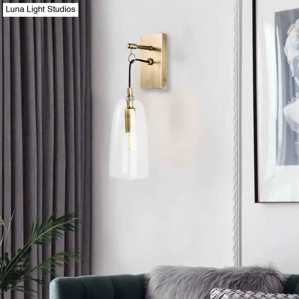Modern brass wall mount lamp with clear glass bell-shaped shade and exposed filament bulb for bedroom lighting