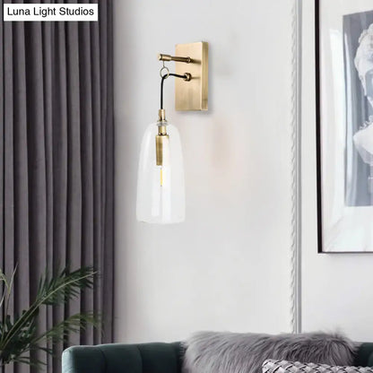 Modern brass wall mount lamp with clear glass bell-shaped shade and exposed filament bulb for bedroom lighting