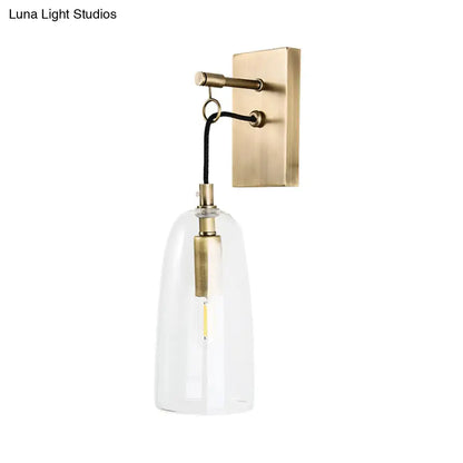 Modern brass wall mount lamp with clear glass bell-shaped shade and exposed led bulb for bedroom lighting
