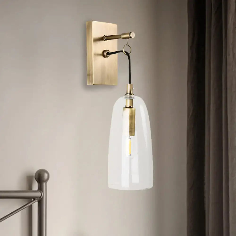 A sleek brass wall mount lamp with a clear glass bell-shaped shade and exposed filament bulb for bedroom use