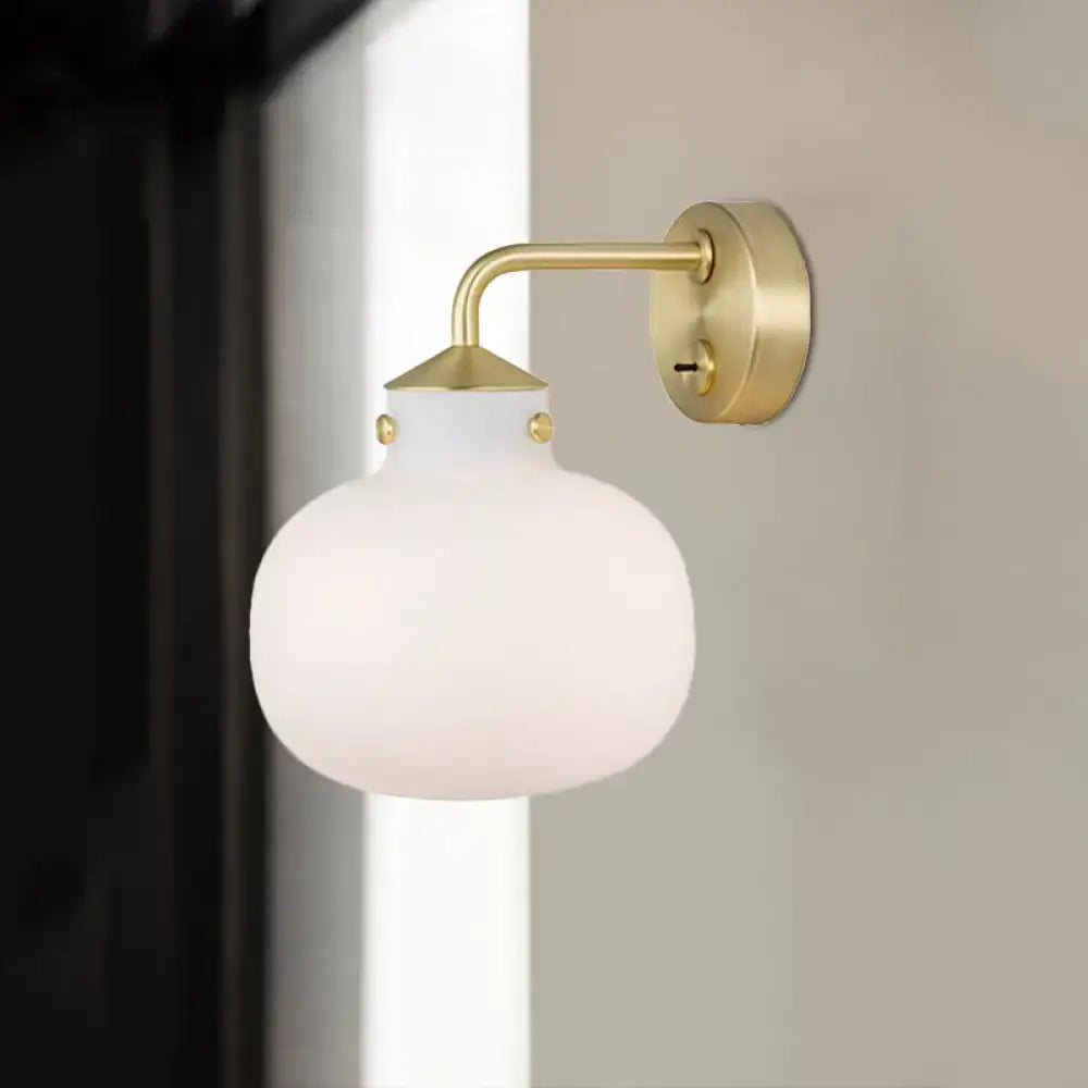 A modern brass wall sconce with an oblong milk white glass shade and decorative gold-toned rivets