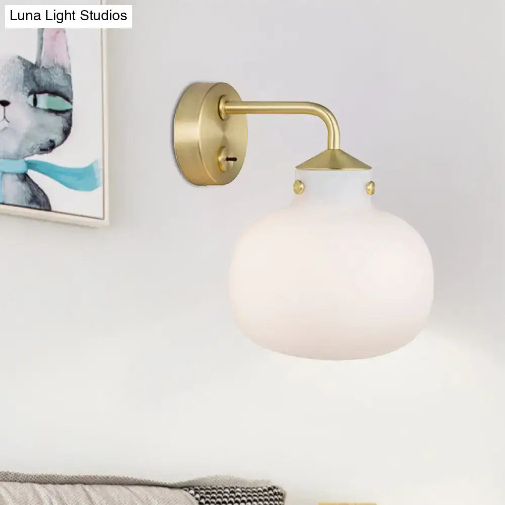 A modern brass wall sconce with oblong milk white glass shade and decorative gold toned accents for balcony lighting