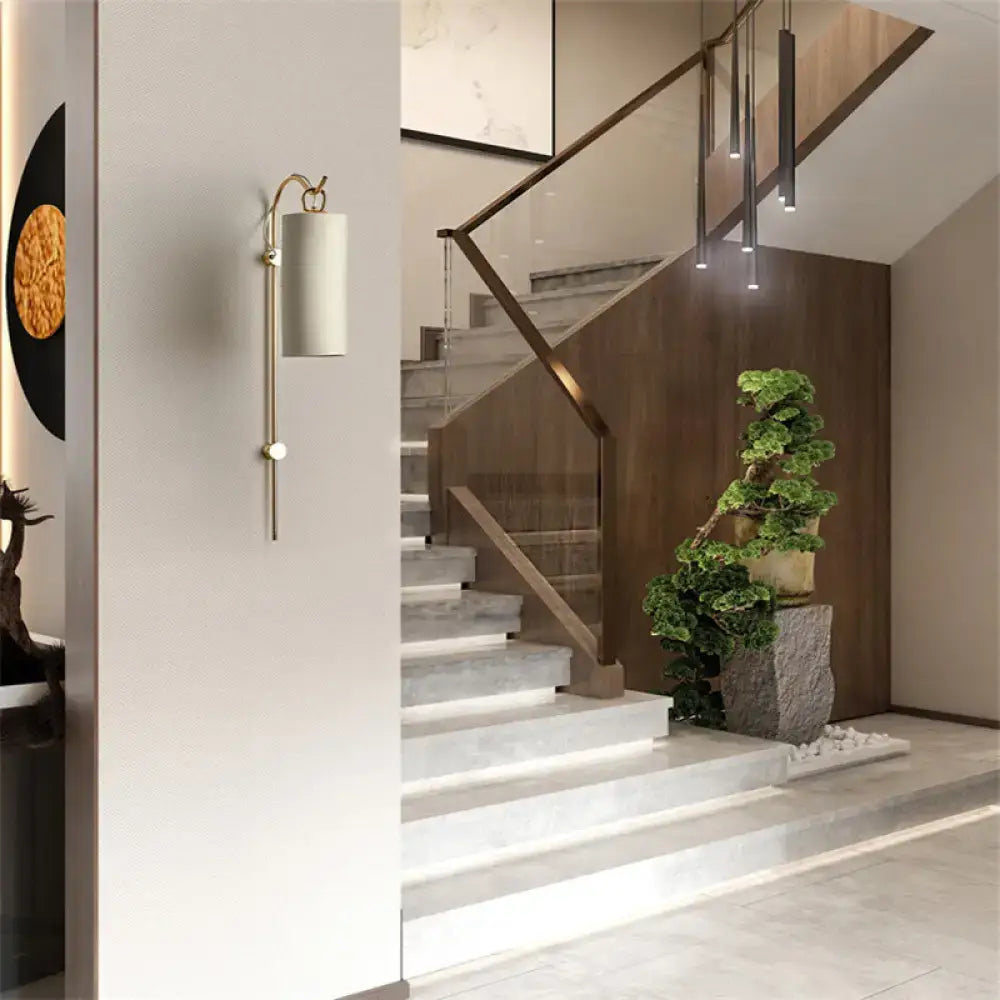 A modern brass and white wall sconce with a cylindrical shade and direct wired electric 220v-240v design