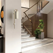 A modern brass and white wall sconce with a cylindrical shade and direct wired electric 220v-240v design