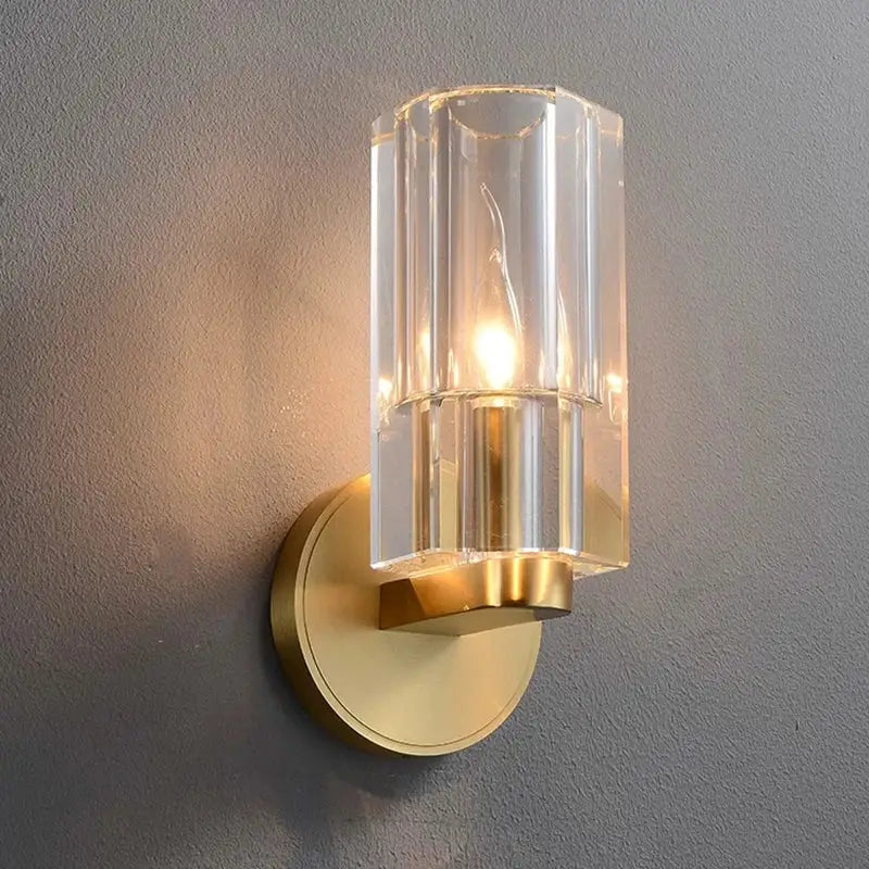 A modern wall lamp with a clear faceted glass cylinder and gold-toned decorbites bronze copper crystal base