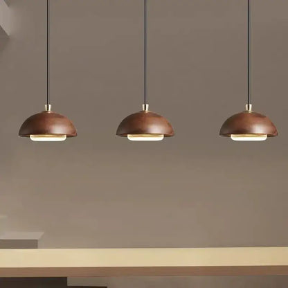 Three modern pendant lights with warm matte copper dome shades and black cords for kitchen island brown finish