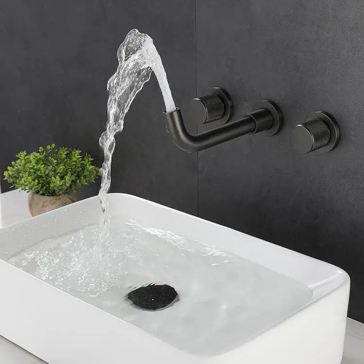 Black matte wall-mounted basin faucet with textured knobs and curved spout pouring water into white sink decorbites brushed gold alternative