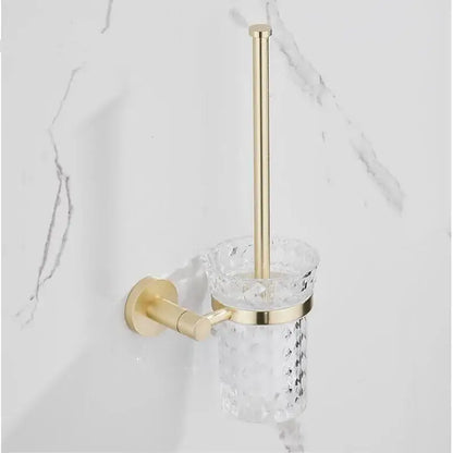 Modern brushed gold bathroom hardware set featuring a gold-toned toilet brush holder with faceted glass cup and brass wall mount