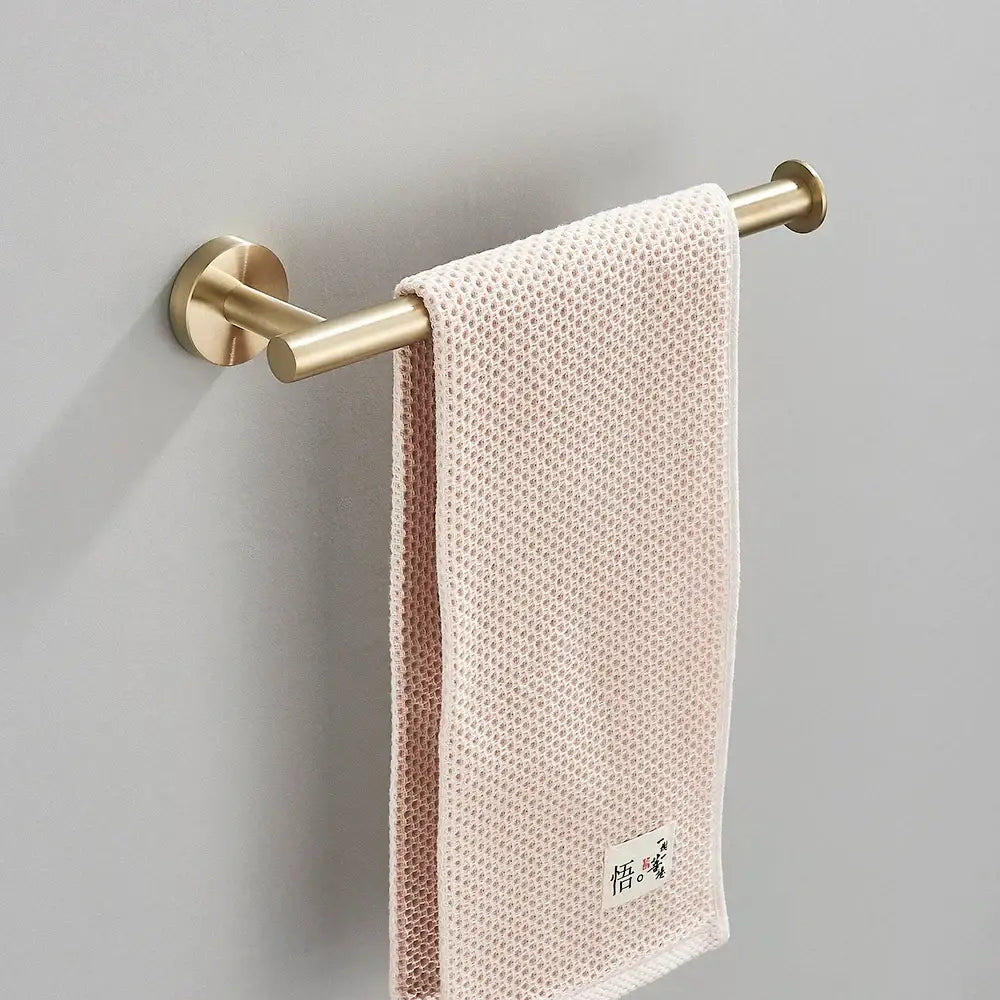 A soft blush pink towel hangs on a decorbites brushed gold hardware set with double-bar towel rack for brushed gold bathroom decor