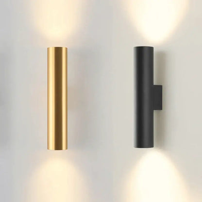 Modern brushed gold and matte black cylindrical wall lamps emitting a warm glow for bedroom lighting use