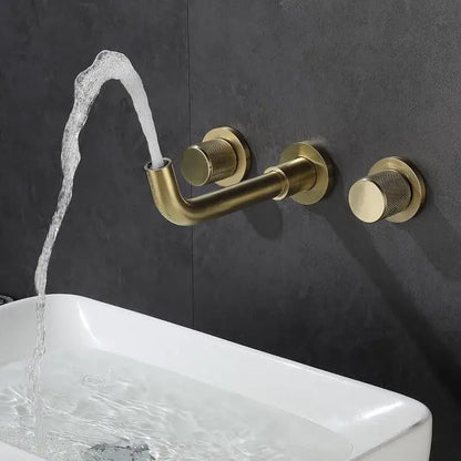 Modern brushed gold wall mount faucet with textured knobs and curved spout flowing water into white sink
