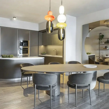 Modern oval dining table with light wood top and minimalist metal legs beneath decorbites candy glass ceiling chandelier