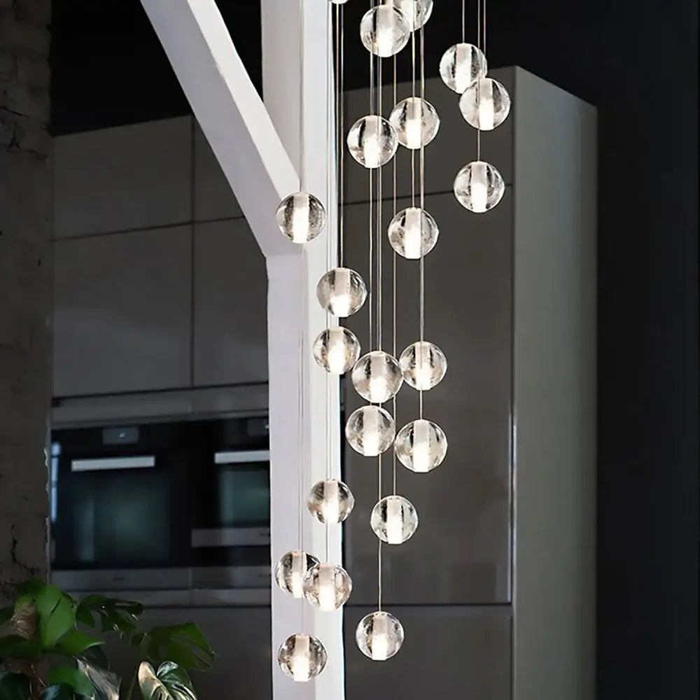 Modern cascading crystal ball led pendant light features a glass sphere chandelier with clear faceted bulbs and metallic chains