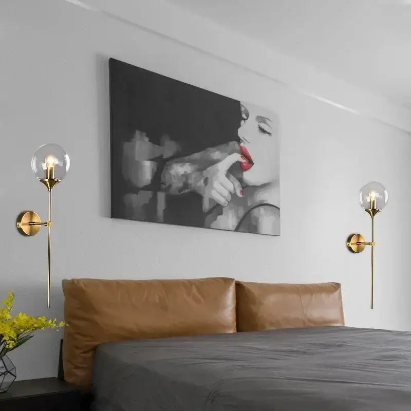 Black-and-white canvas artwork of woman with red lips and tattooed arms above bed with modern chrome and amber glass ball wall lamps decorbites glass ball lighting