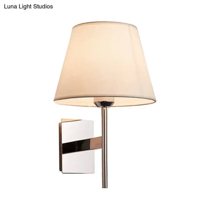 Modern wall light featuring a chrome-finished metal arm and cream fabric cone shade for bedroom use