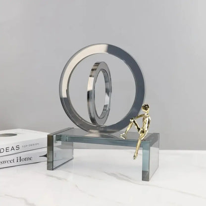 A sleek modern chrome sculpture with geometric crystal rings and a small golden man for living room decor