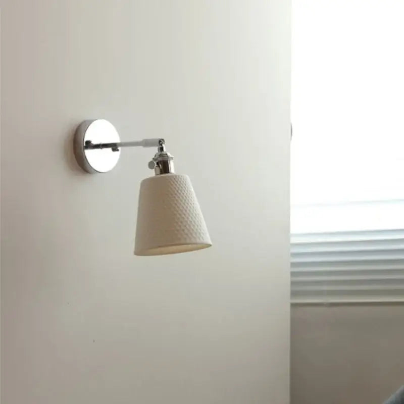 Modern chrome wall light fixture with off-white perforated ceramic lampshade and polished chrome arm for bedroom use