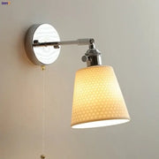 Modern chrome and perforated fabric wall light fixture with warm-toned lampshade and polished chrome arm for bedroom use