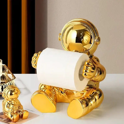 Golden astronaut tissue box holder with shiny metallic finish designed to hold white tissue paper roll in living room