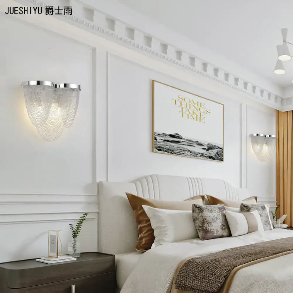 Modern chrome wall light with a silver frame and cascading clear crystal strands for bedroom use
