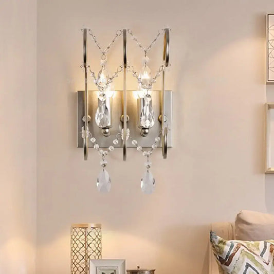 A modern chrome crystal wall sconce light type with polished chrome frame and dangling crystal teardrops for bedroom
