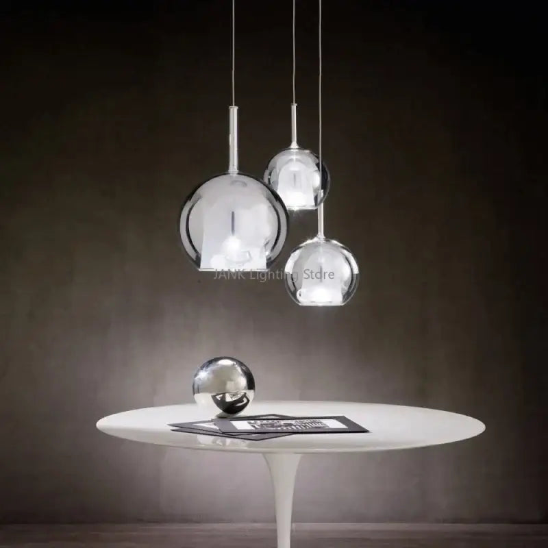 Modern chrome glass bubble pendant lights with spherical design hang above a white table for dining room decorbites