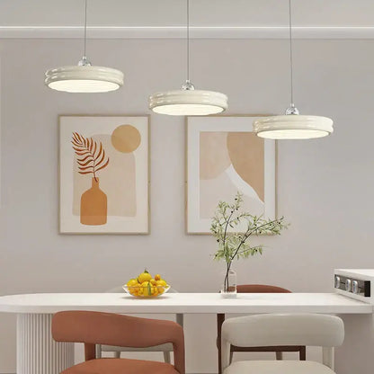 Three modern pendant lights with circular pale yellow ceramic shades form a decorbites circular modern chandelier