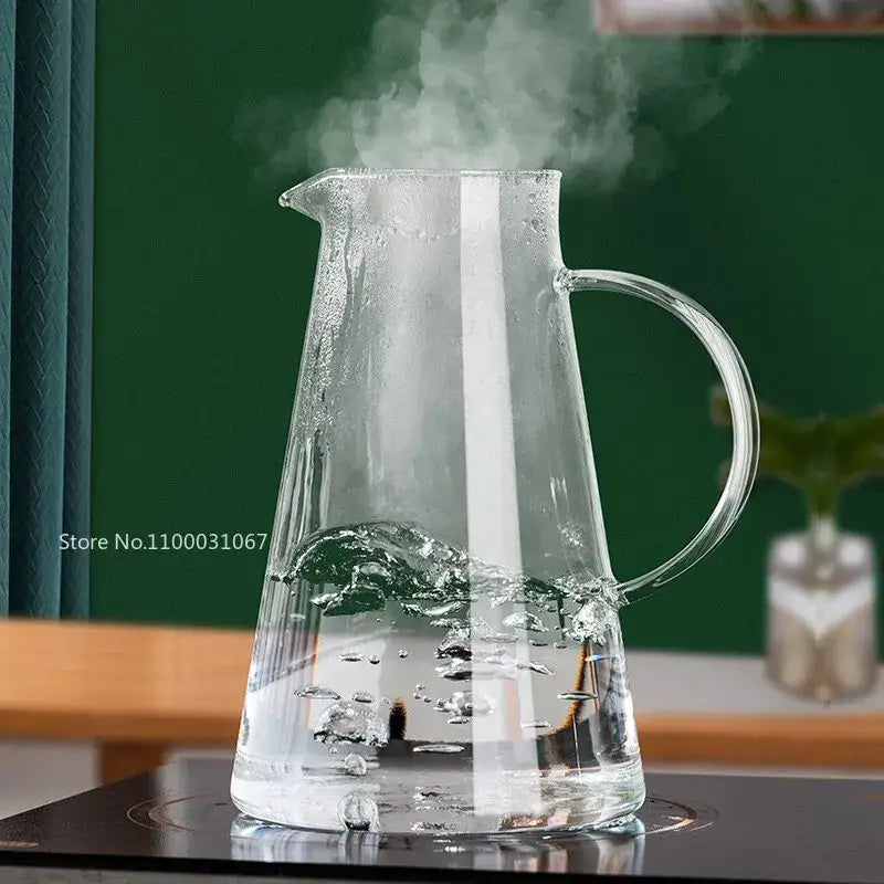 Modern clear borosilicate glass pitcher with stainless steel lid filled with steaming water and curved handle