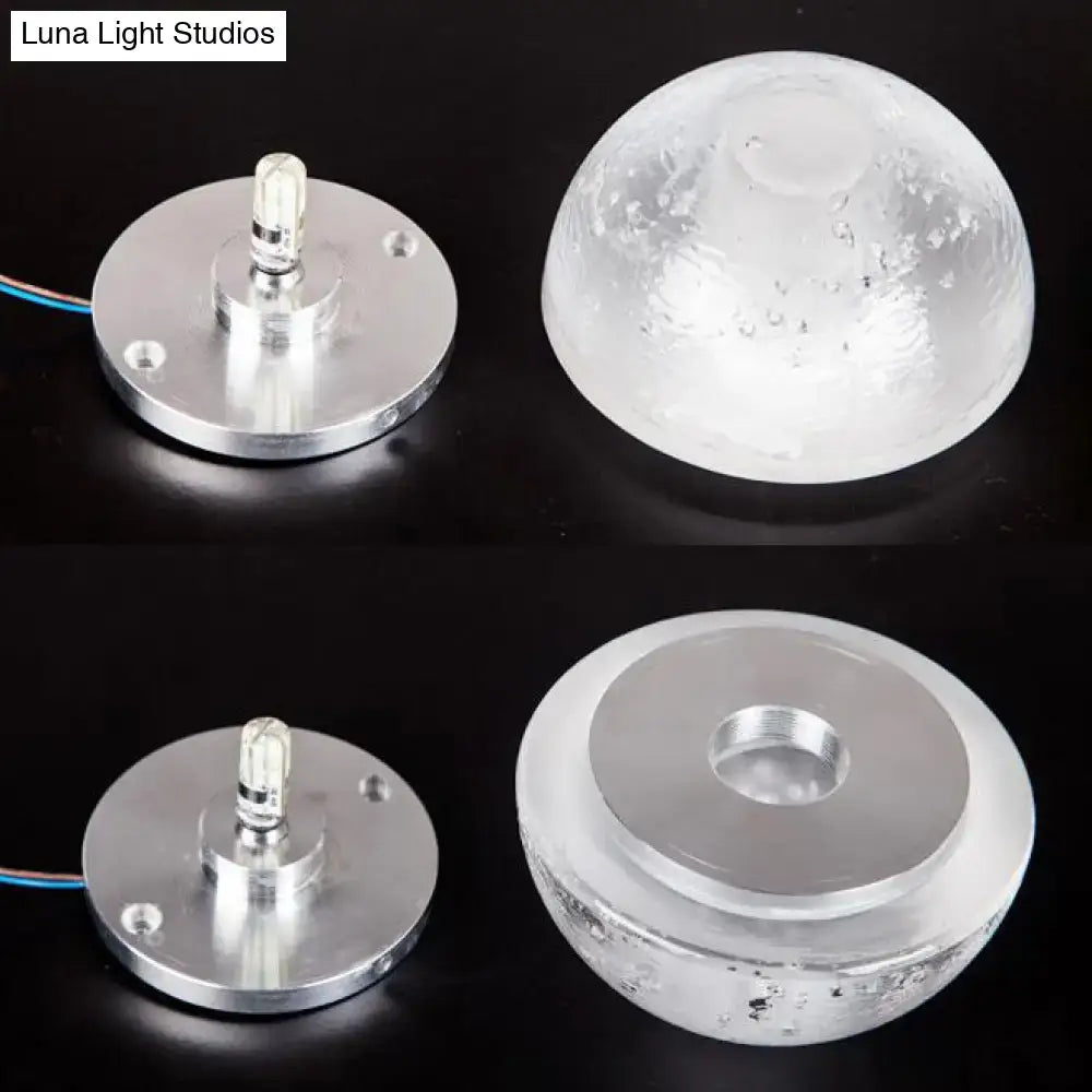 Modern wall light with clear bubble crystal textured dome and silver base emitting warm white light for living room use