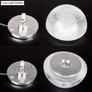 Modern wall light with clear bubble crystal textured dome and silver base emitting warm white light for living room use
