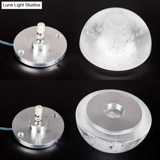Modern wall light with clear bubble crystal textured dome and silver base emitting warm white light for living room use