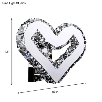 A modern clear crystal heart wall lamp with faceted edges and a mirrored center by luna light studios emitting warm white light