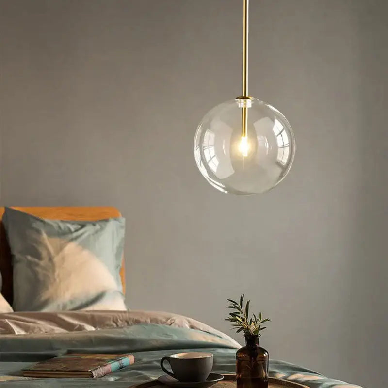 Modern pendant light featuring a clear transparent glass globe with a brass-finished gold kitchen rod suspension