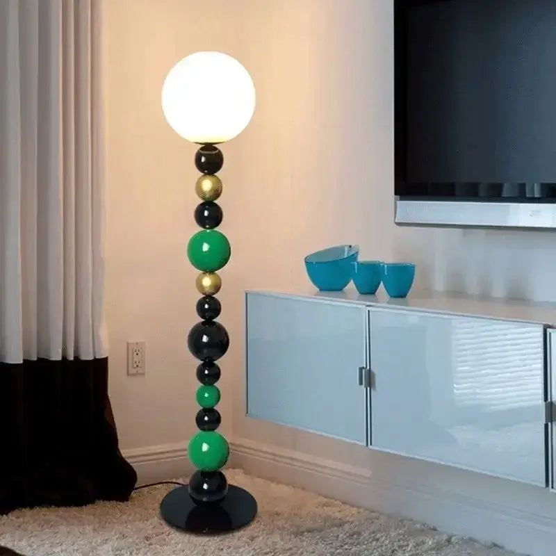A modern floor lamp with colorful glass balls in black green and gold featuring a glowing white spherical bulb for living room