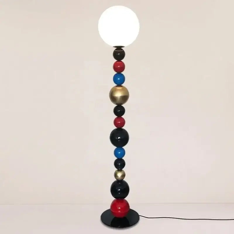 A modern floor lamp with colorful glass ball spheres in red blue black and gold and a white globe bulb for living room