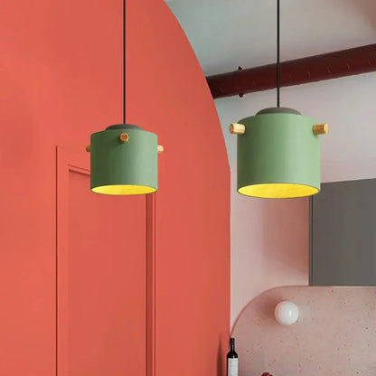 Two cylindrical green decorbites colorful led pendant lights with brass accents hang against a coral wall for dining room decor