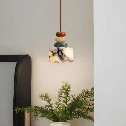A modern pendant lamp with decorbites colorful stone orbs in red beige and teal above a white marble shade for dining decor