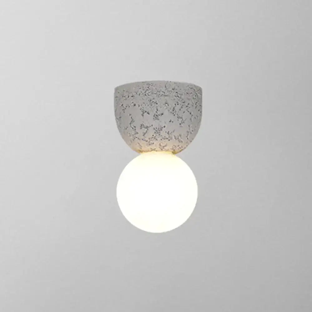Modern concrete bell wall-mounted light fixture with speckled gray finish and glowing white spherical bulb for bedroom sconce