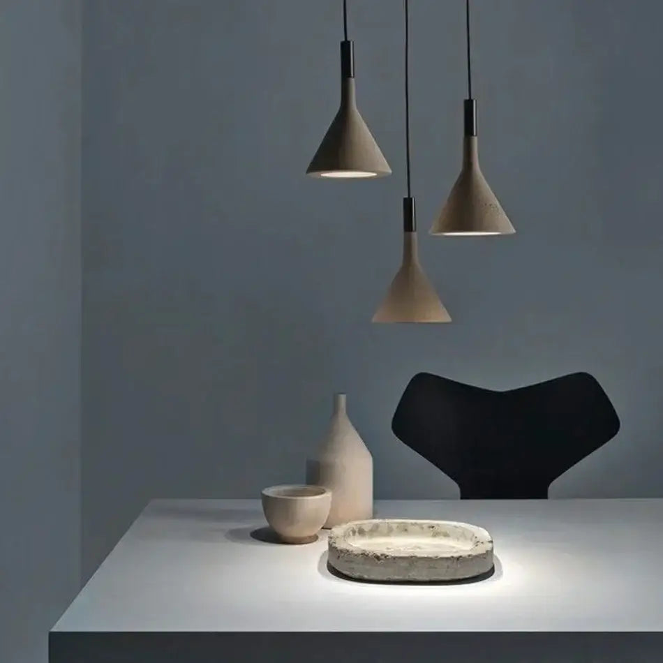 Three minimalist gray concrete pendant lights with conical shades hang on black cords for kitchen decorbites pendant lights