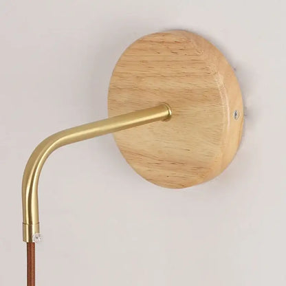 Modern copper and wood wall sconce with round wooden backplate, curved brass arm, and clear glass pull chain switch