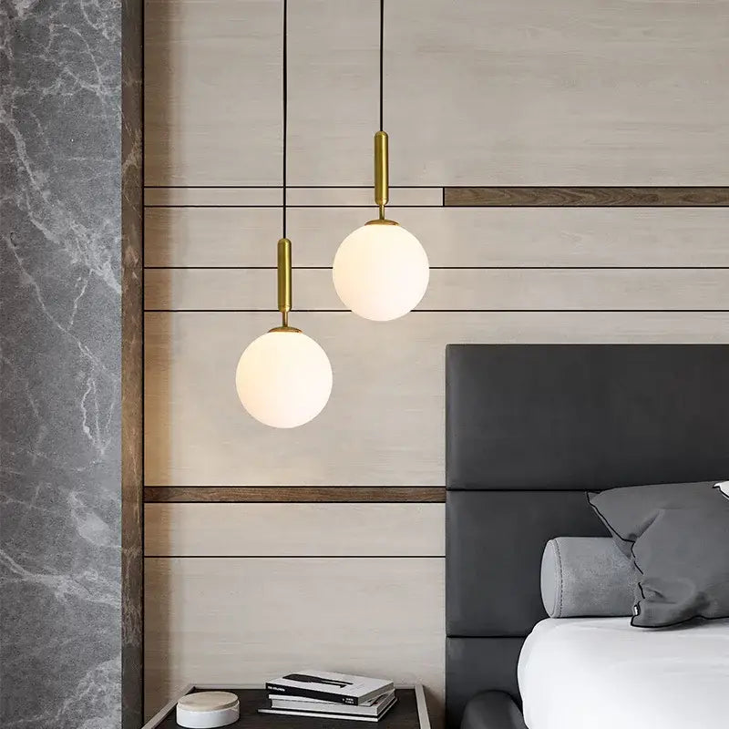 Two cream glass planet pendant lights with brass fixtures hang from black cords in a modern bedroom pendant light design