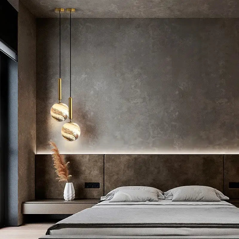 Modern cream and blue glass planet pendant light with spherical marbled shades and gold fixtures hanging above bed