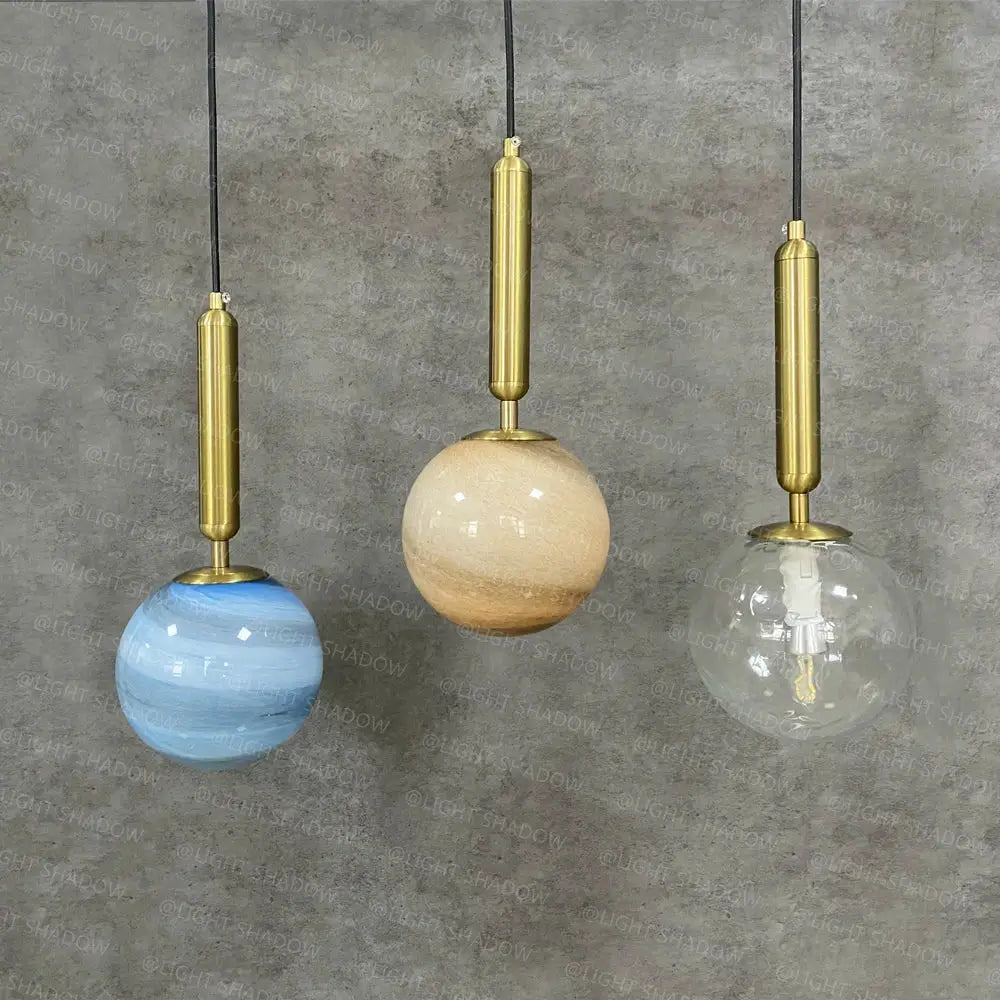 Three modern pendant lights with brass fixtures and blue beige clear glass planet shades for bedroom use