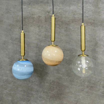 Three modern pendant lights with brass fixtures and blue beige clear glass planet shades for bedroom use